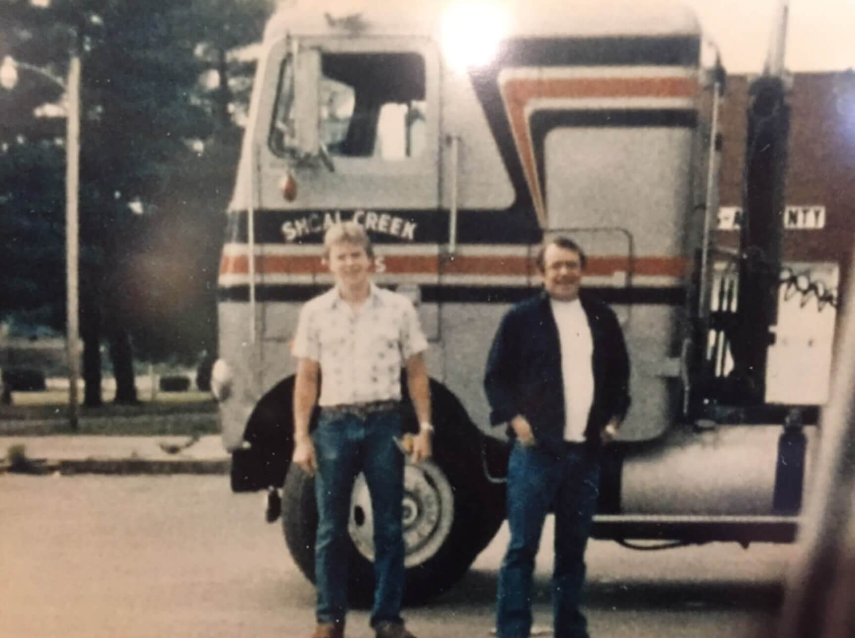70s photo of two men standing in front of truck cab