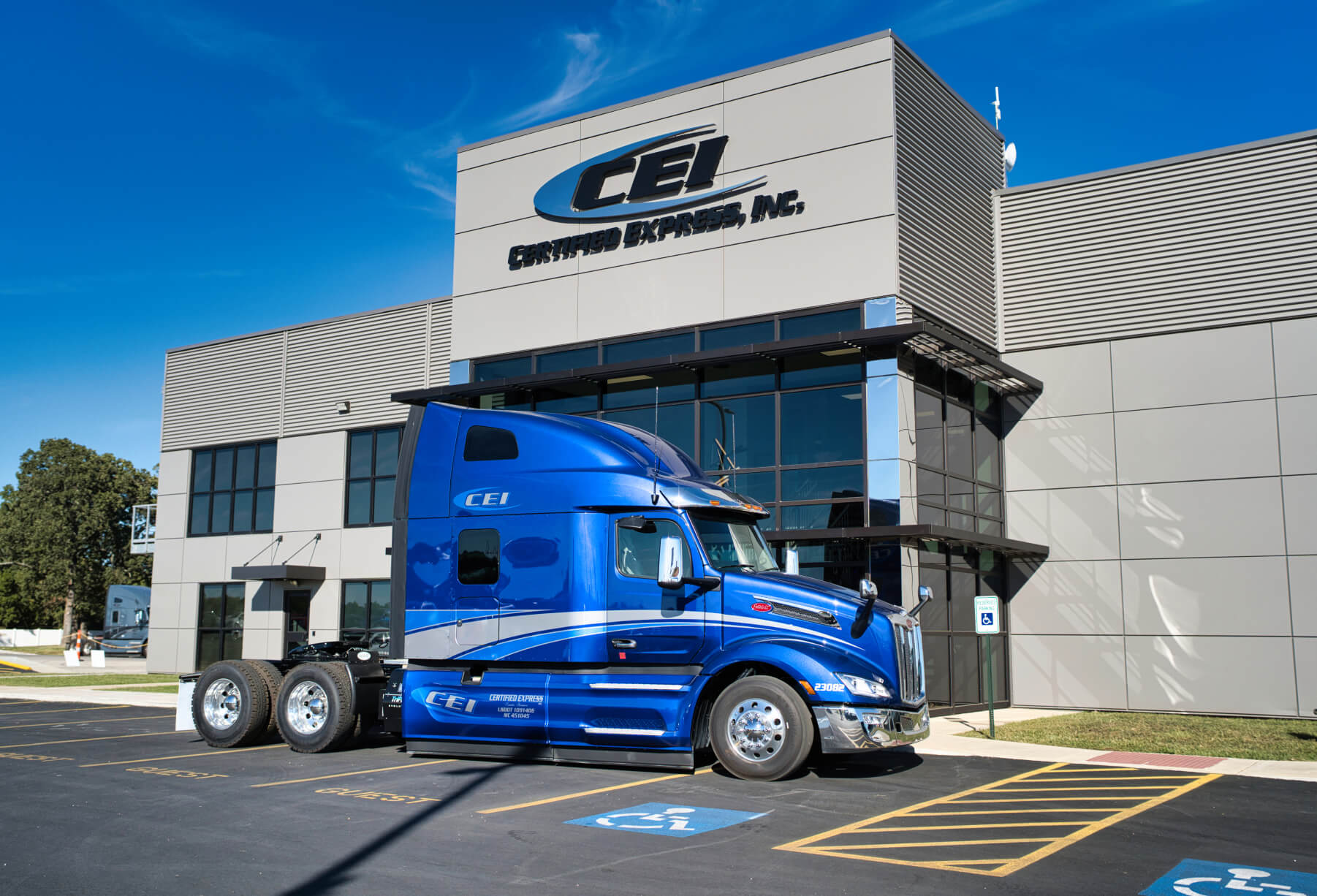A gleaming blue CEI semi truck is parked in front of headquarters under a clear blue sky.
