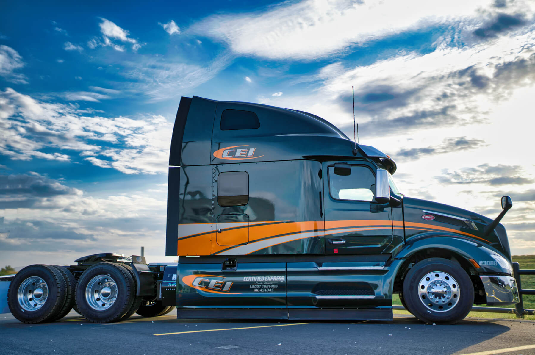 A gleaming black CEI truck with an orange stripe shown in profile against a clear blue sky.