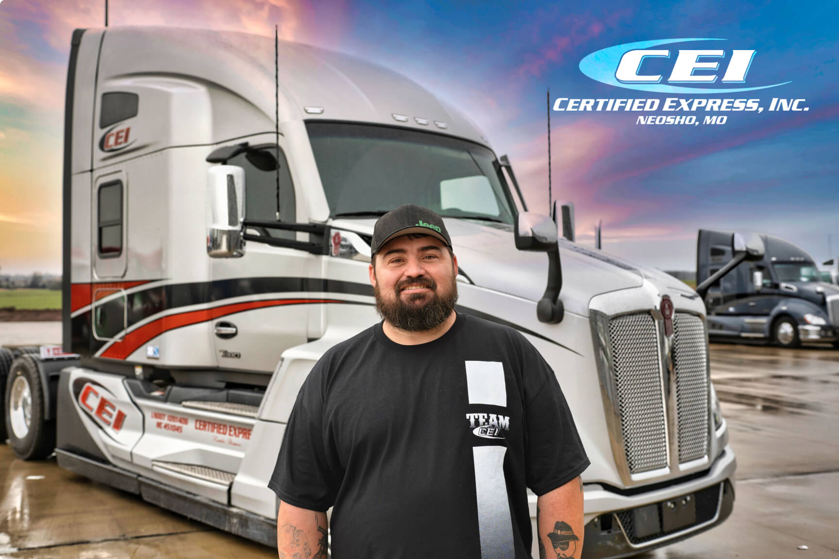 A male CEI employee wearing a black hat stands in front of a silver semi truck .