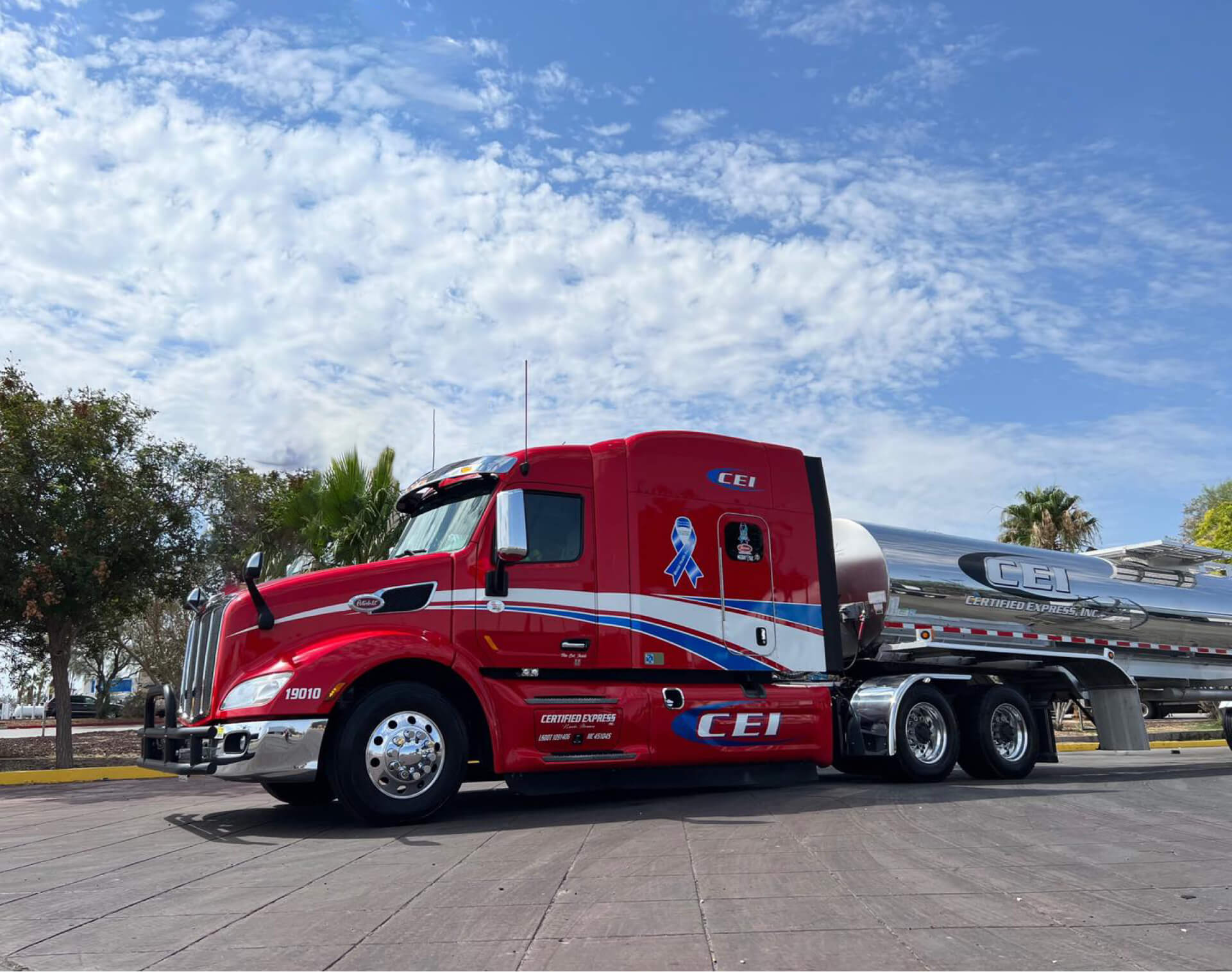 A red CEI truck with pneumatic trailer is parked on pavement in front of a blue sky.