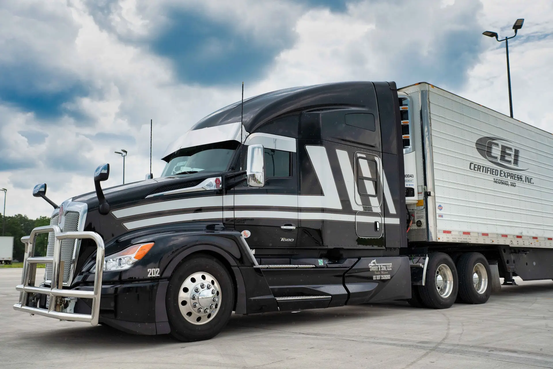 A black semi-truck with white stripes is parked at a lot, attached to a white CEI Certified Express trailer under a cloudy sky.